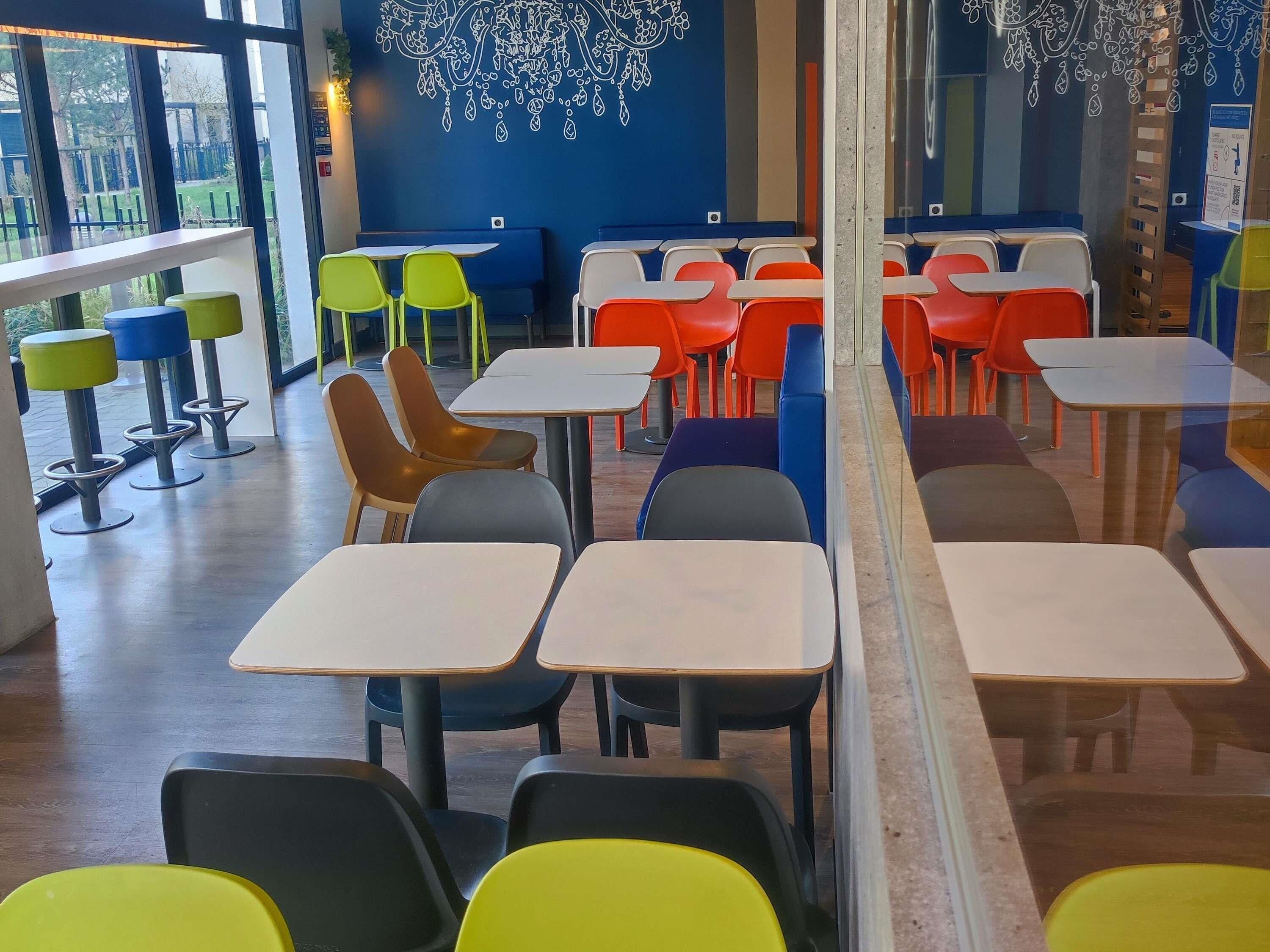 A dining area with tables and chairs, a blue wall with a white pattern, and a view through a window.