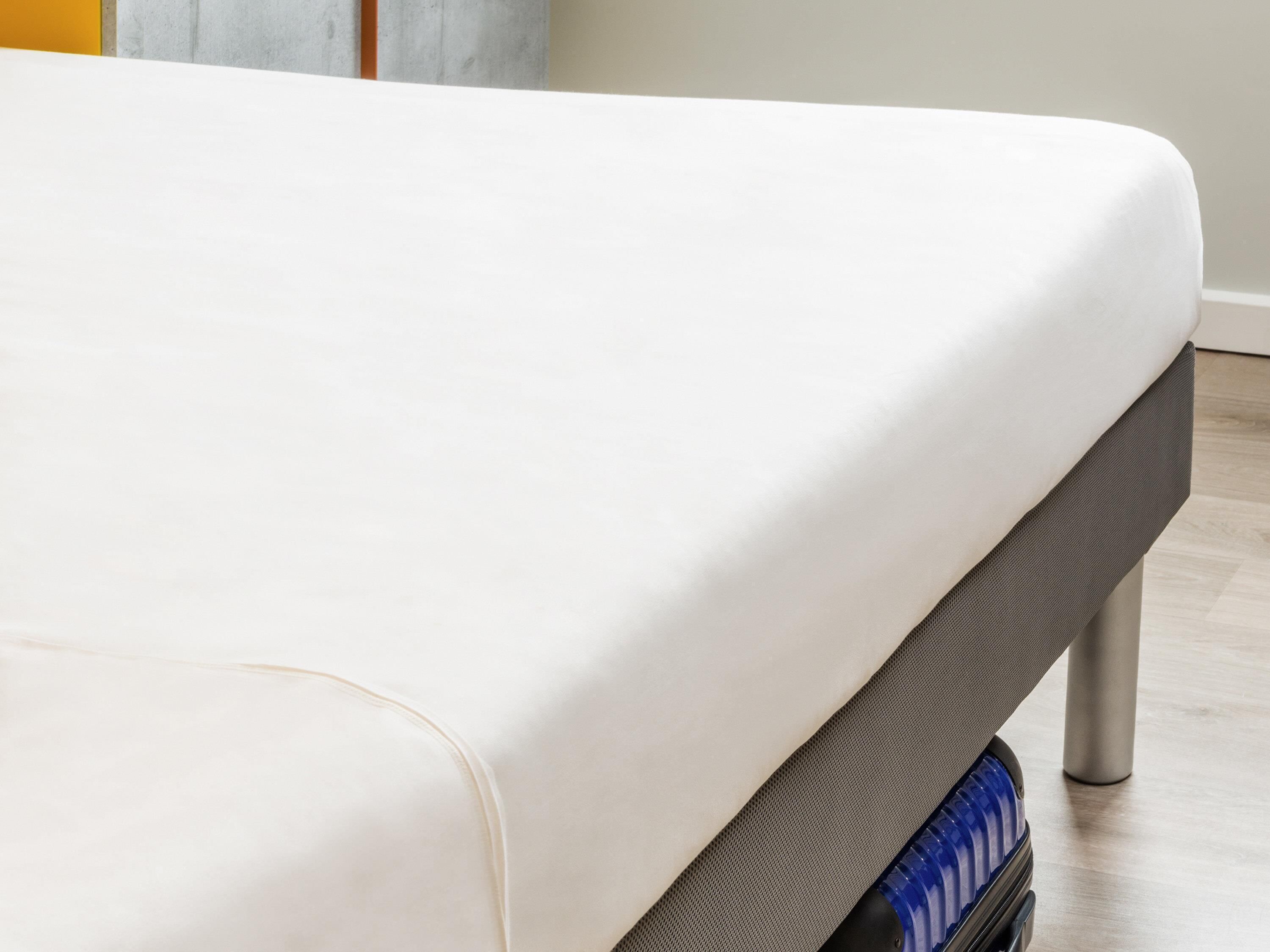 A bed with a white mattress and a grey headboard.