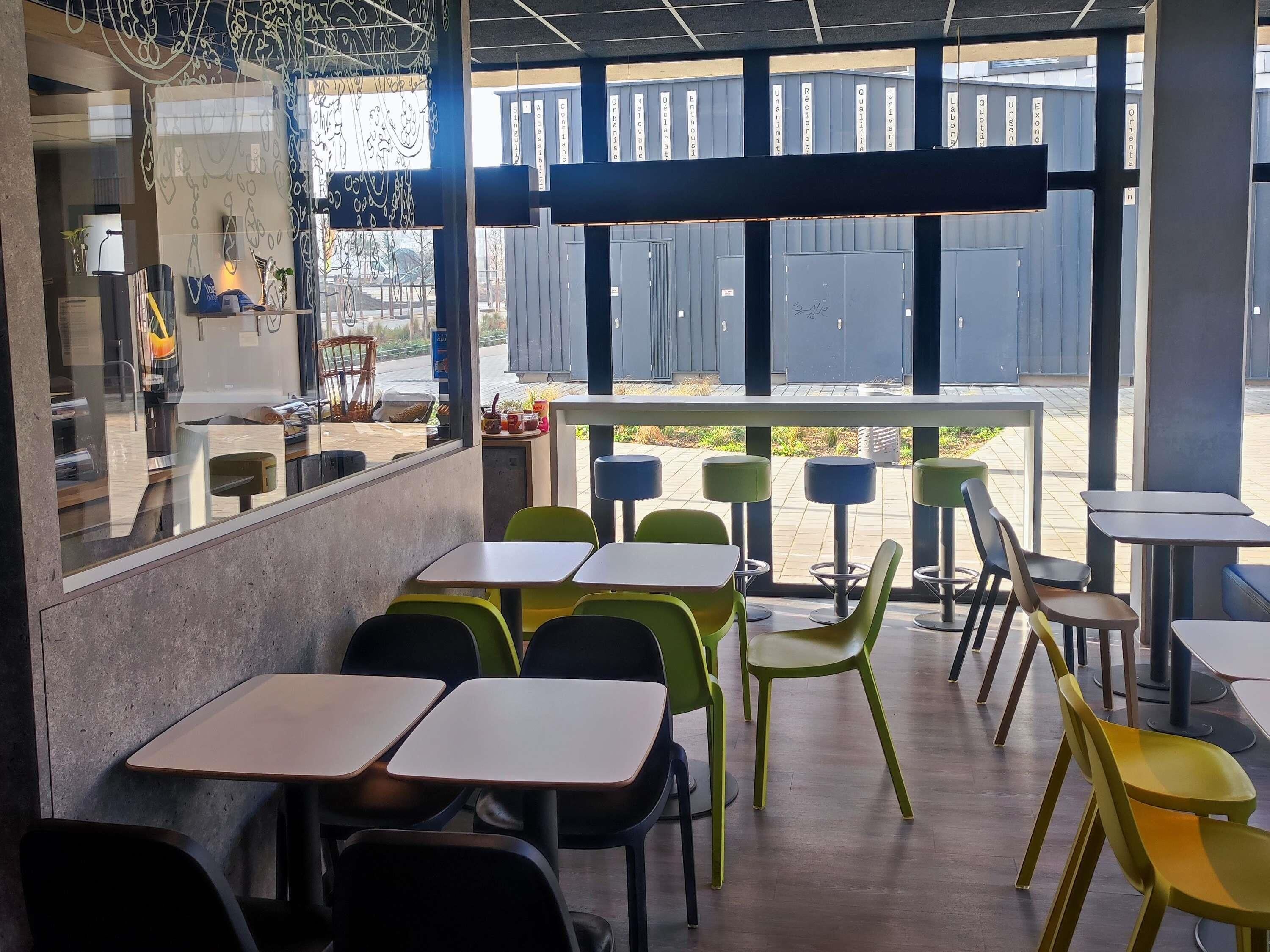 Un café moderne avec une terrasse, de grandes fenêtres et une vue sur la rue.