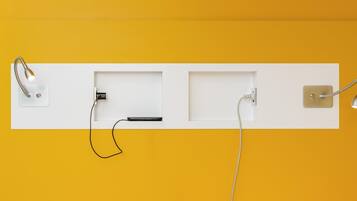 A wall-mounted electrical outlet with a power strip, a phone charging, and a lamp.