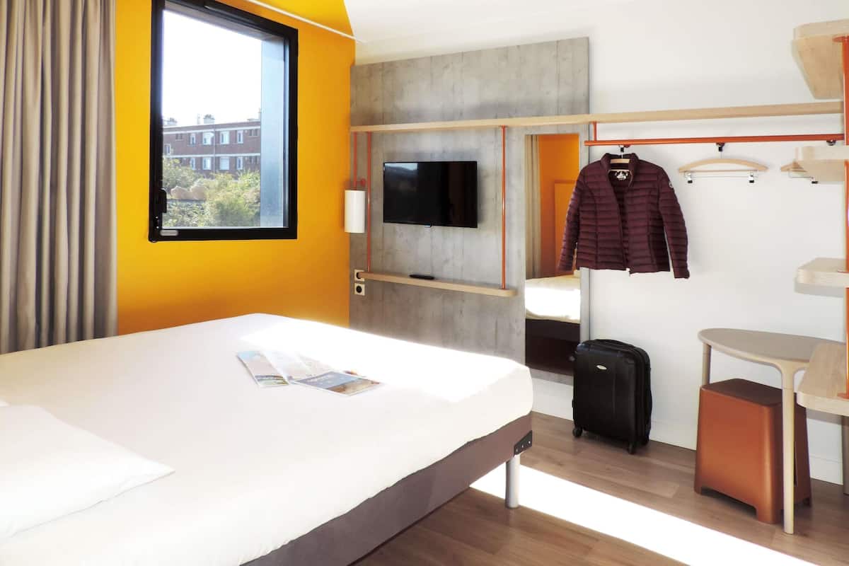 Une chambre d’hôtel avec un lit, une télévision, un porte-manteau et une valise.
