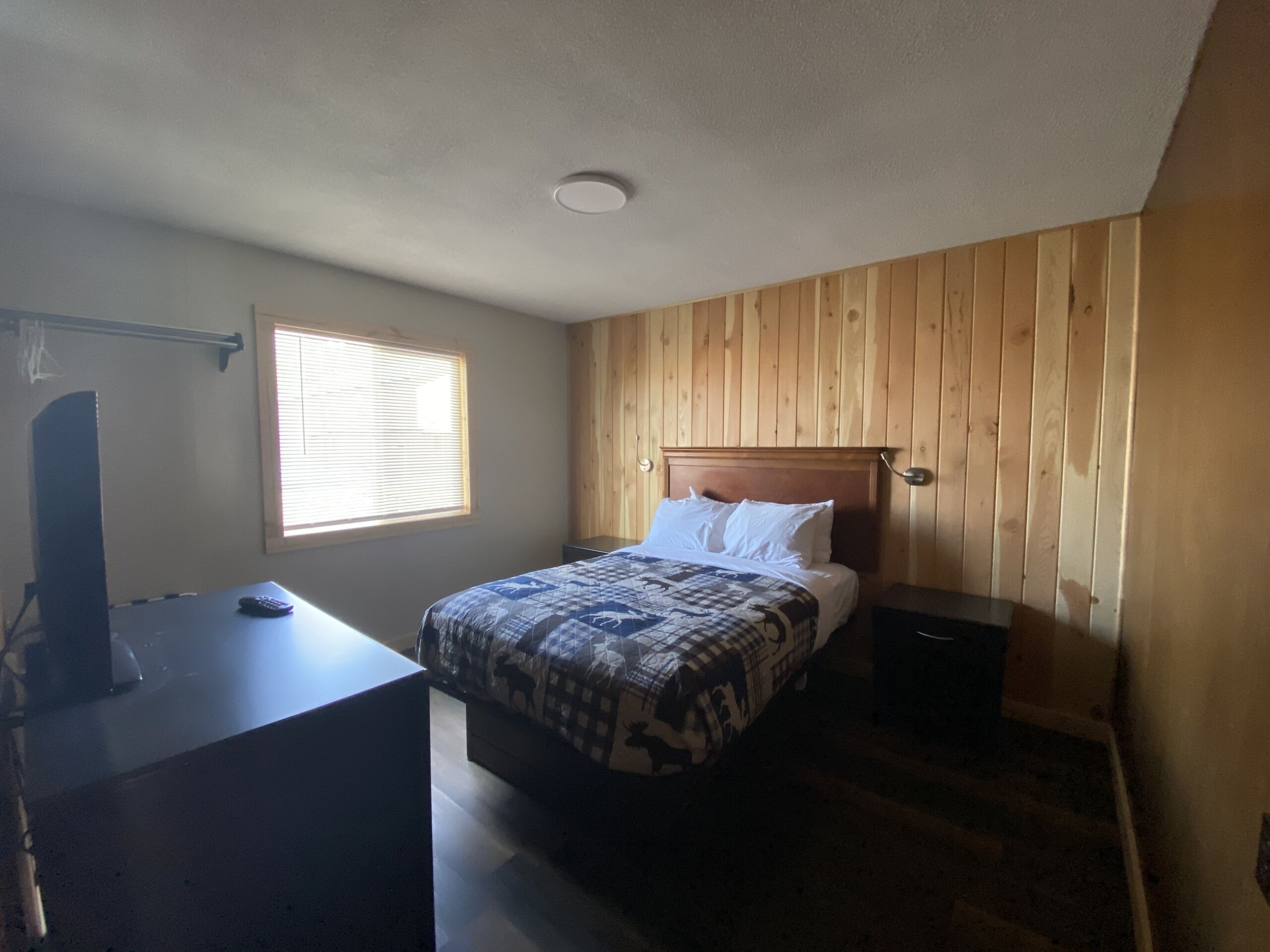 Un dormitorio con cama, escritorio, televisor y ventana con persianas.