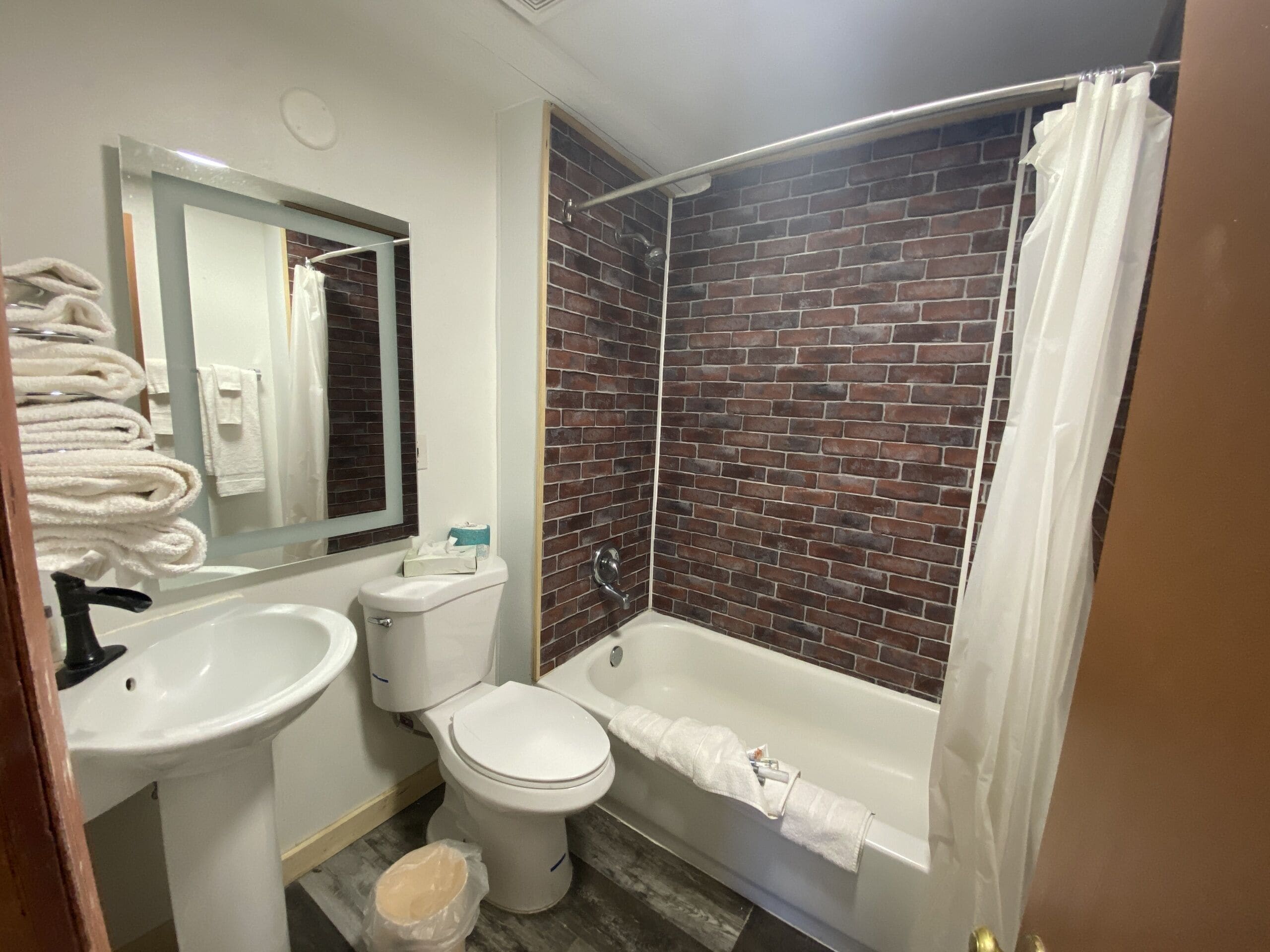 Une salle de bain avec un lavabo, des toilettes et une baignoire, tous de couleur blanche. Un miroir est placé au-dessus du lavabo et un rideau de douche est installé au-dessus de la baignoire.