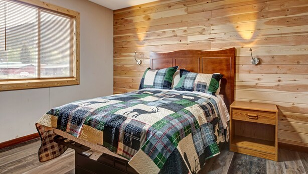 Une chambre à coucher avec une tête de lit en bois, une couvre-lit matelassée, une table de chevet et une fenêtre avec des stores.