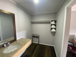 Un baño con lavamanos de granito, un espejo, toallero y estante con toallas dobladas.