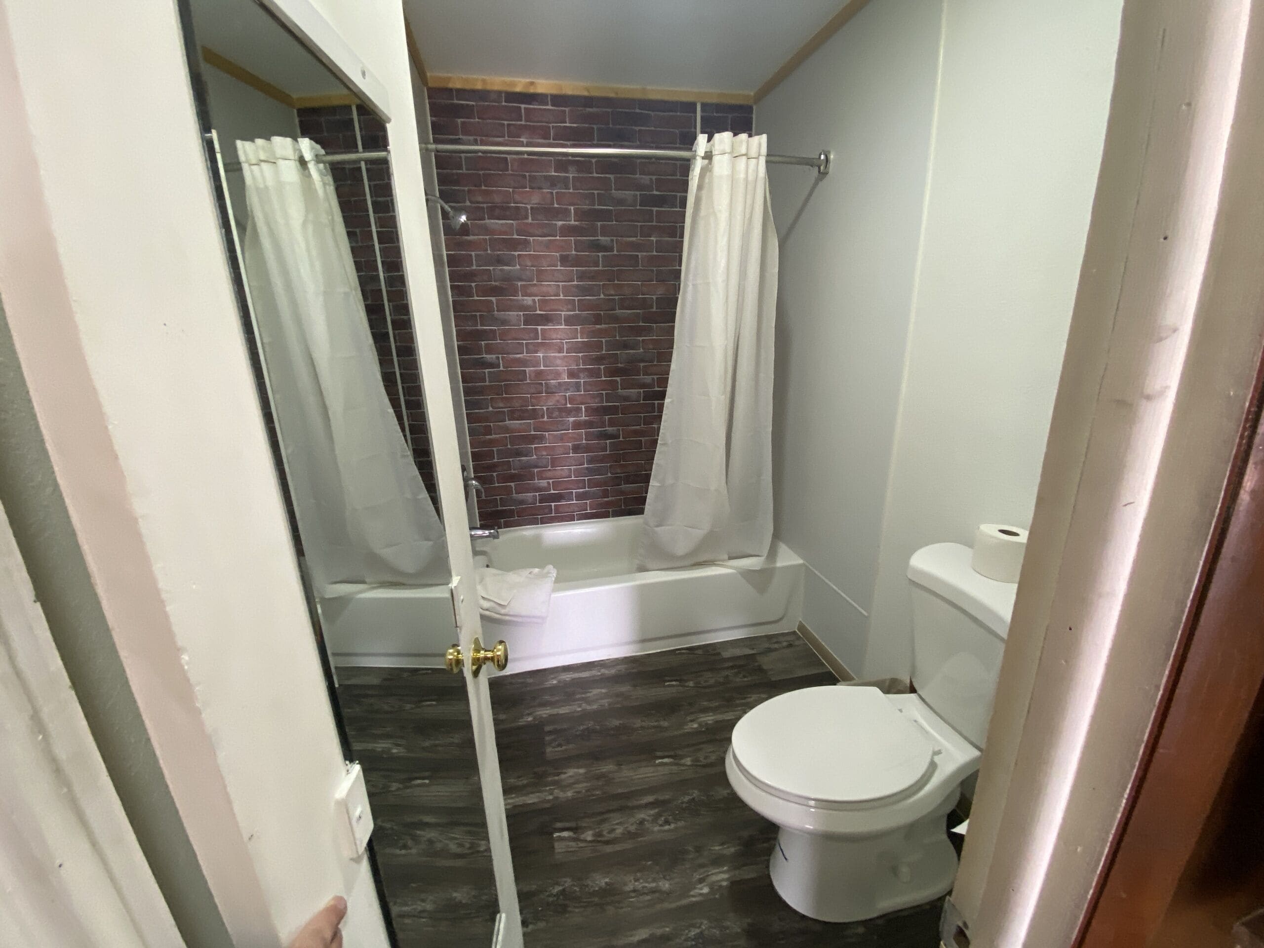 A small bathroom with a shower, toilet, and a brick wall.