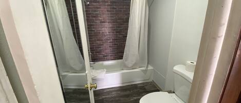 A small bathroom with a shower, toilet, and a brick wall.