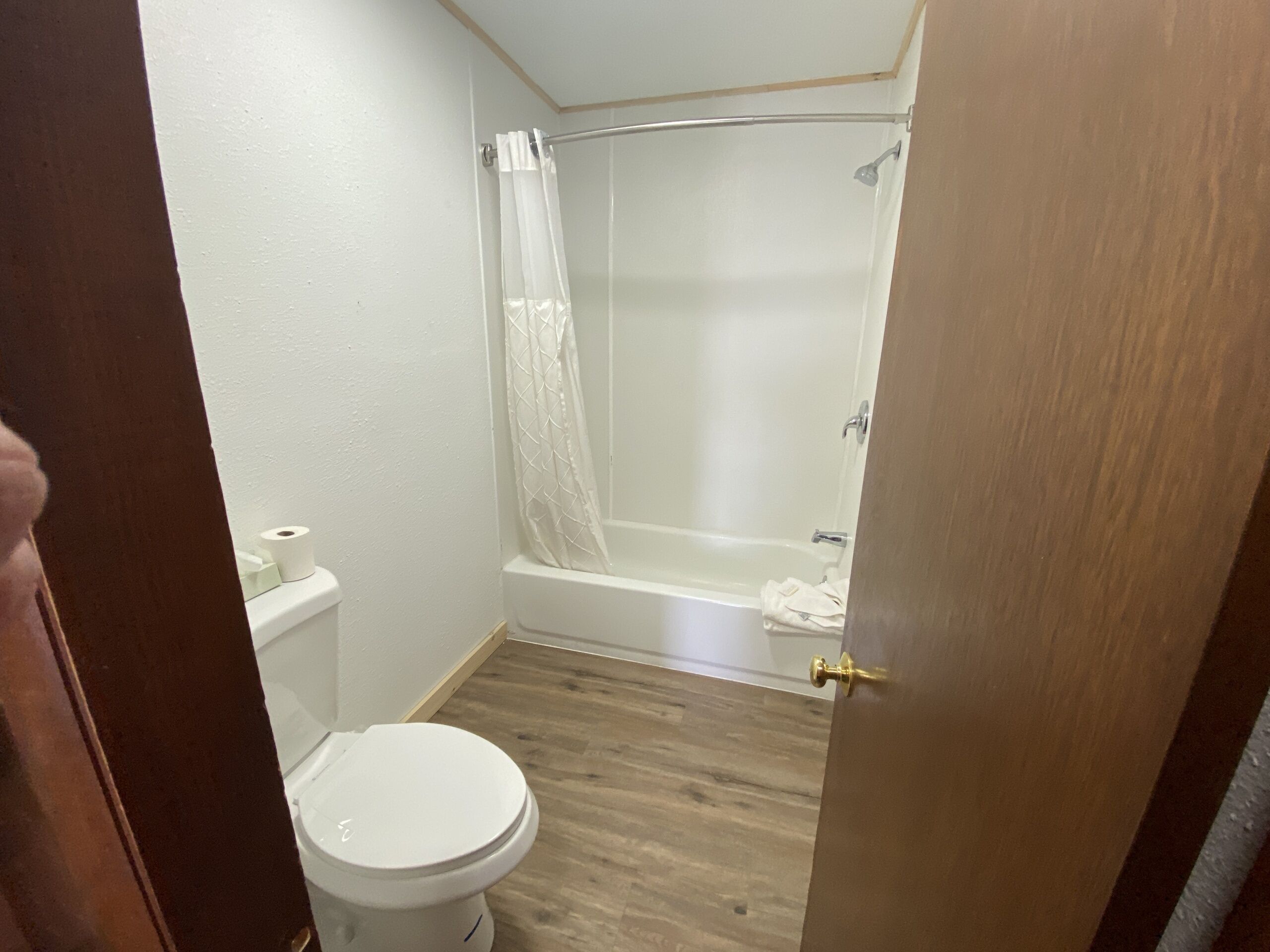 A bathroom with a toilet, a shower with a glass door, and a wooden floor.