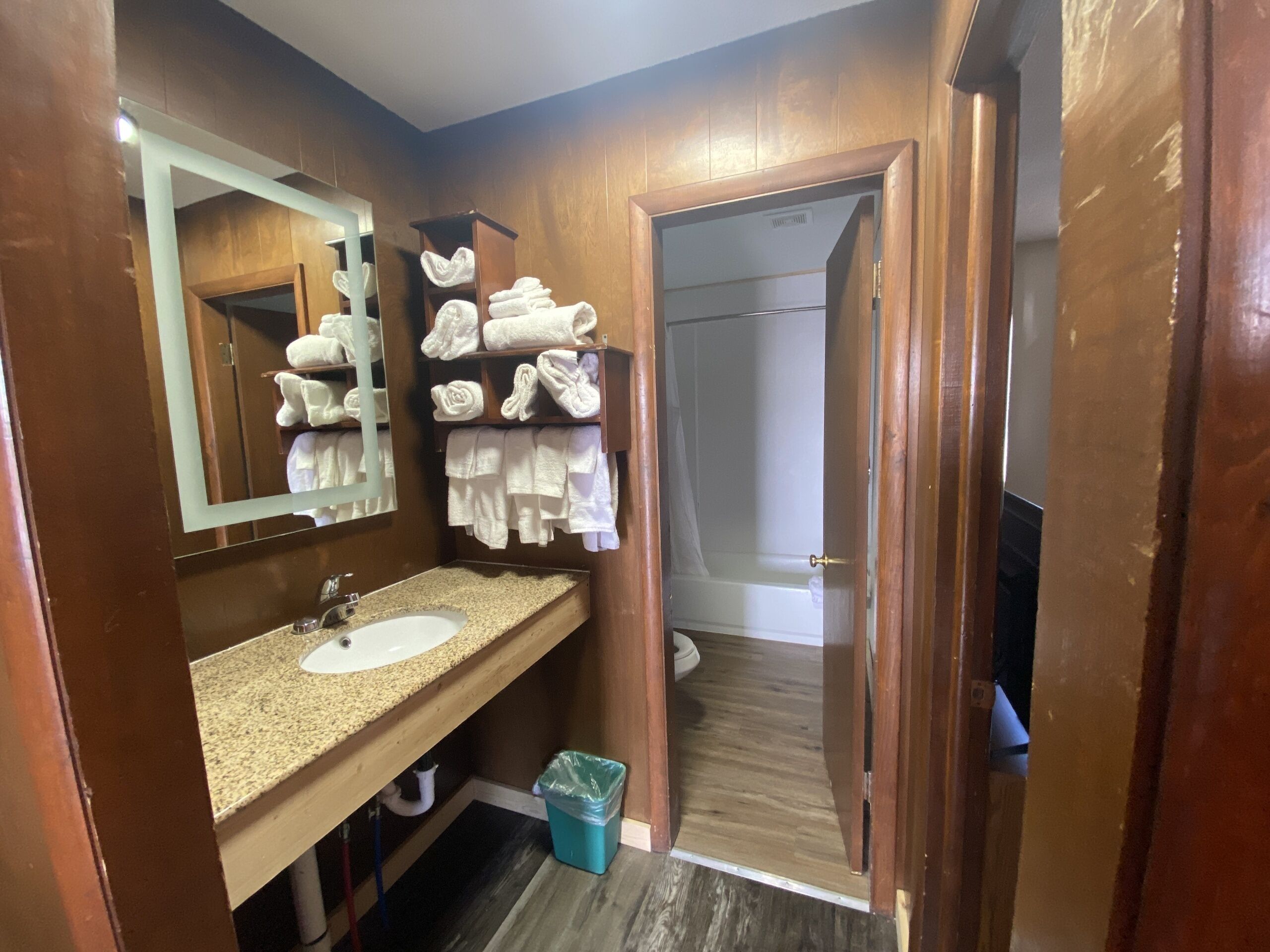 A bathroom with a sink, mirror, towel rack, and a door leading to a shower area.
