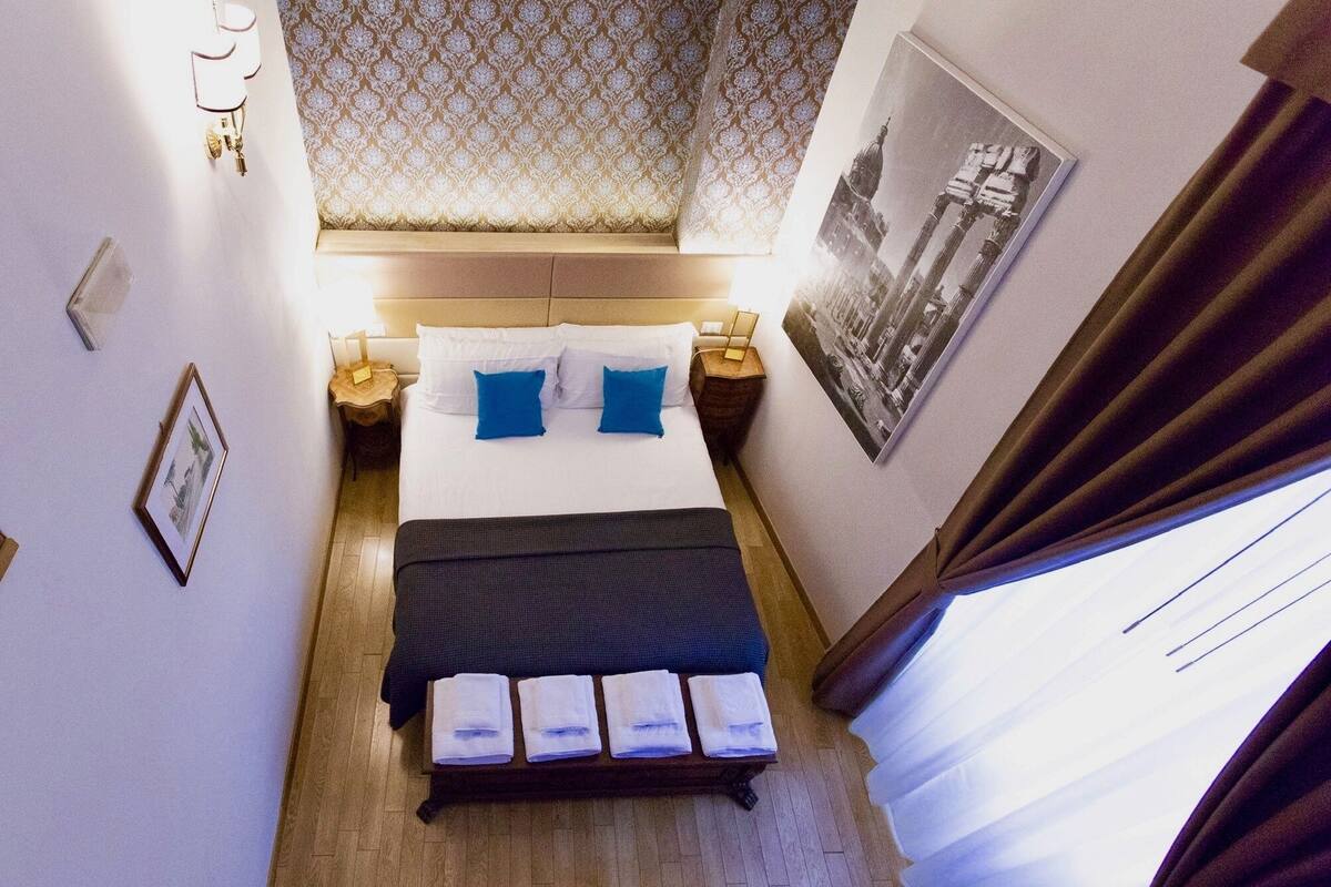 A hotel room with a bed, bedside lamps, a nightstand, a framed picture, and a window with curtains.