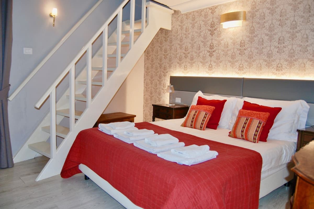 A bedroom with a large bed, a wooden nightstand, a red throw blanket, and a staircase.