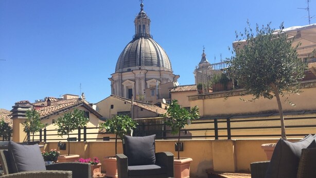 An outdoor seating area with wicker furniture and a glass table, overlooking a historic building with a dome. - Navona Residenza de Charme (Rome)
