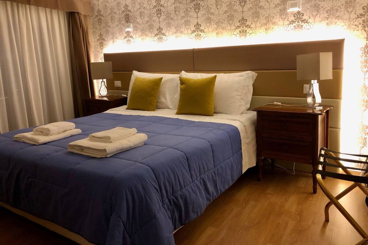 A hotel room with a large bed, a nightstand, a lamp, and a wooden chair.