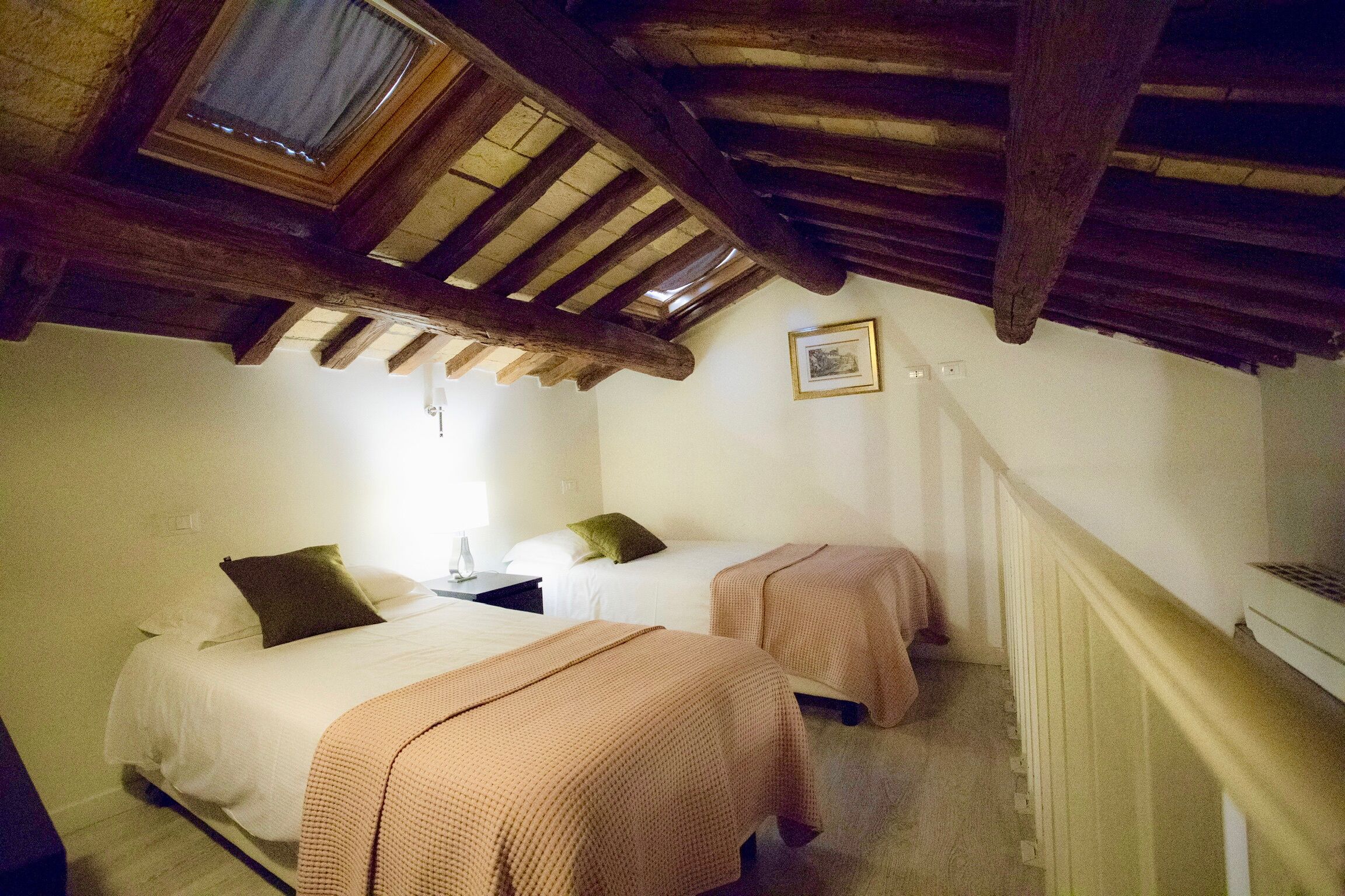 A bedroom with two beds, wooden beams, a window, and a staircase.