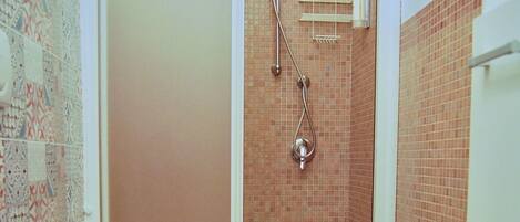 Ein Badezimmer mit Toilette, einer Dusche mit Glastür und einer gefliesten Wand.