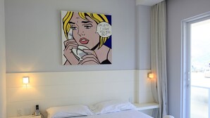 Una camera d'albergo con un letto, lampade sui comodini, un quadro appeso e una finestra con tende.