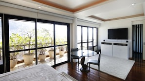A modern room with a large sliding glass door, a round dining table with chairs, a flat-screen TV mounted on the wall, and a potted plant by the window. - Rio034 - Penthouse Arpoador (Rio de Janeiro)