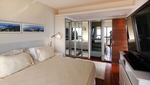 A bedroom with a large bed, a TV, and a view of the bathroom through a glass door. - Rio034 - Penthouse Arpoador (Rio de Janeiro)