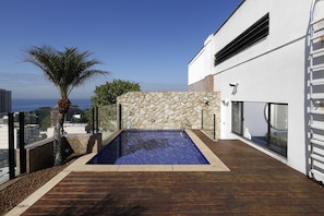 A rooftop pool with a stone wall and wooden deck, overlooking a cityscape. - Rio034 - Penthouse Arpoador (Rio de Janeiro)