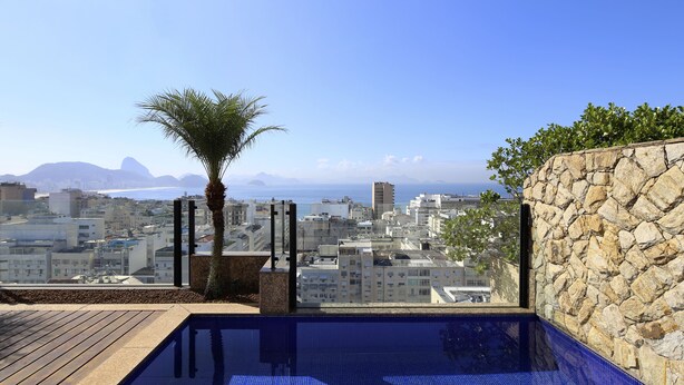 A rooftop pool with a city view, stone wall, and palm tree. - Rio034 - Penthouse Arpoador (Rio de Janeiro)