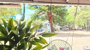 A covered outdoor area with a hanging chair, a potted plant, and a table with a candle. - Acuarela Hostal - Hostel (Rio Hato)