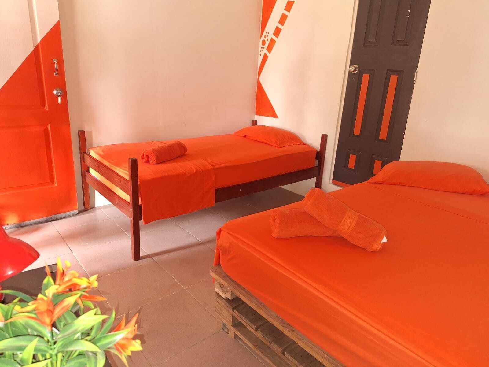 Una habitación con dos camas, cada una con ropa de cama naranja, una puerta de madera y una silla roja.