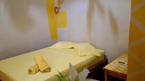A single bed with a yellow bedspread, a rolled towel, and a small wooden table with a remote control. - Acuarela Hostal - Hostel (Rio Hato)
