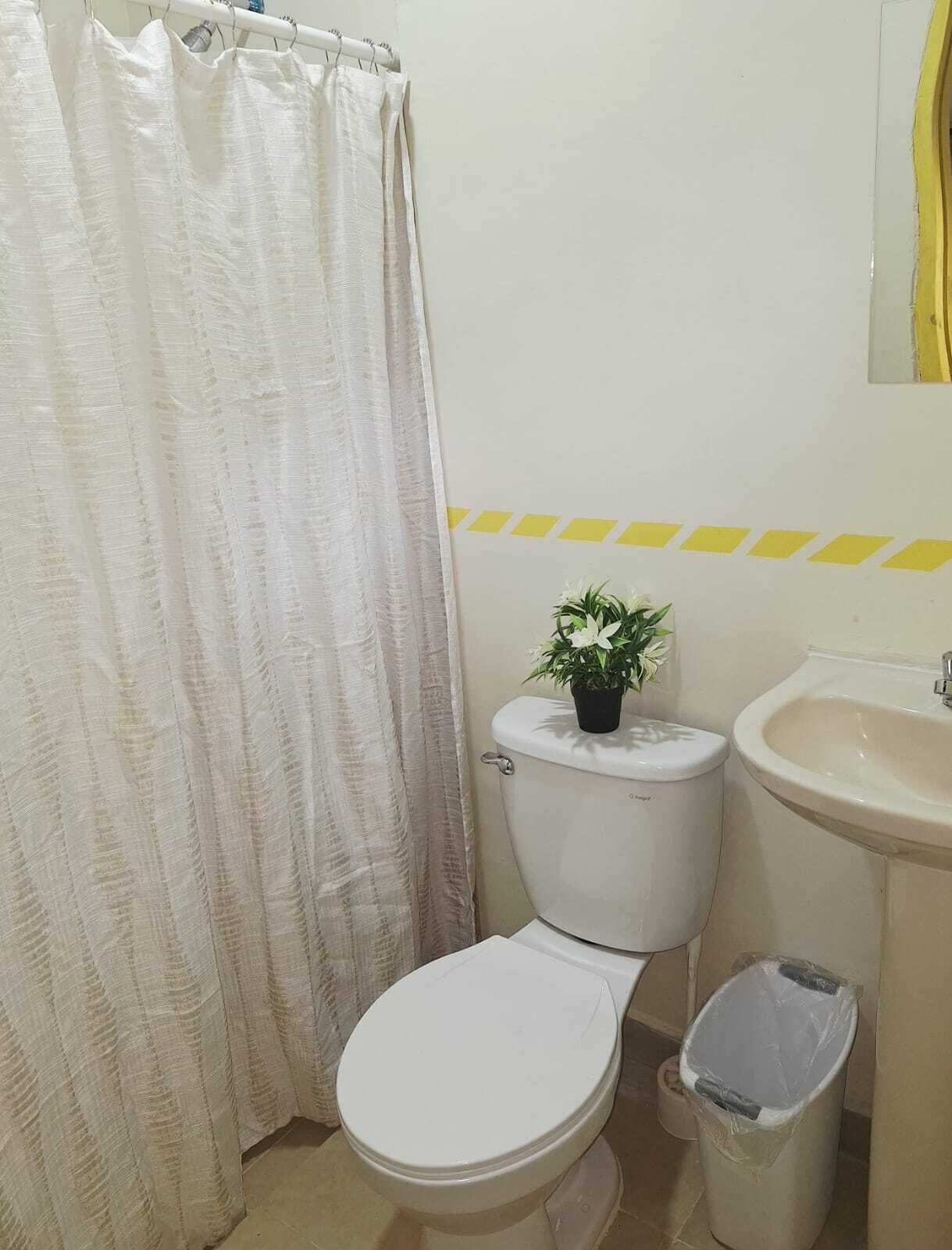 Un baño con inodoro, lavamanos, cubo de basura y cortina de ducha.