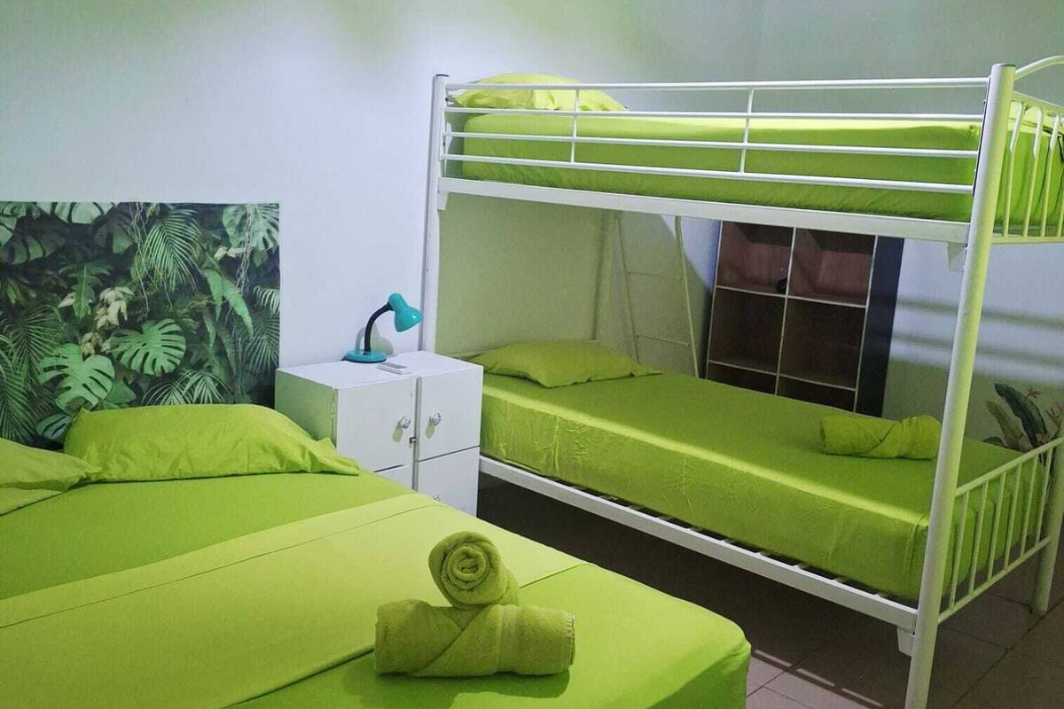 Una habitación con literas, un pequeño aparador blanco y una pared cubierta de plantas verdes.