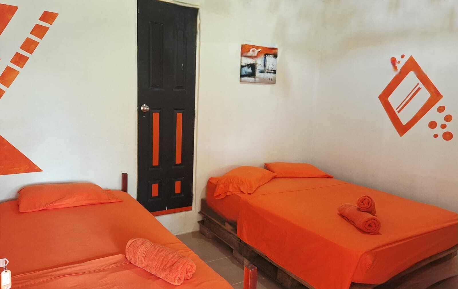 Une chambre avec deux lits, une porte et un mur orné d’un petit tableau.