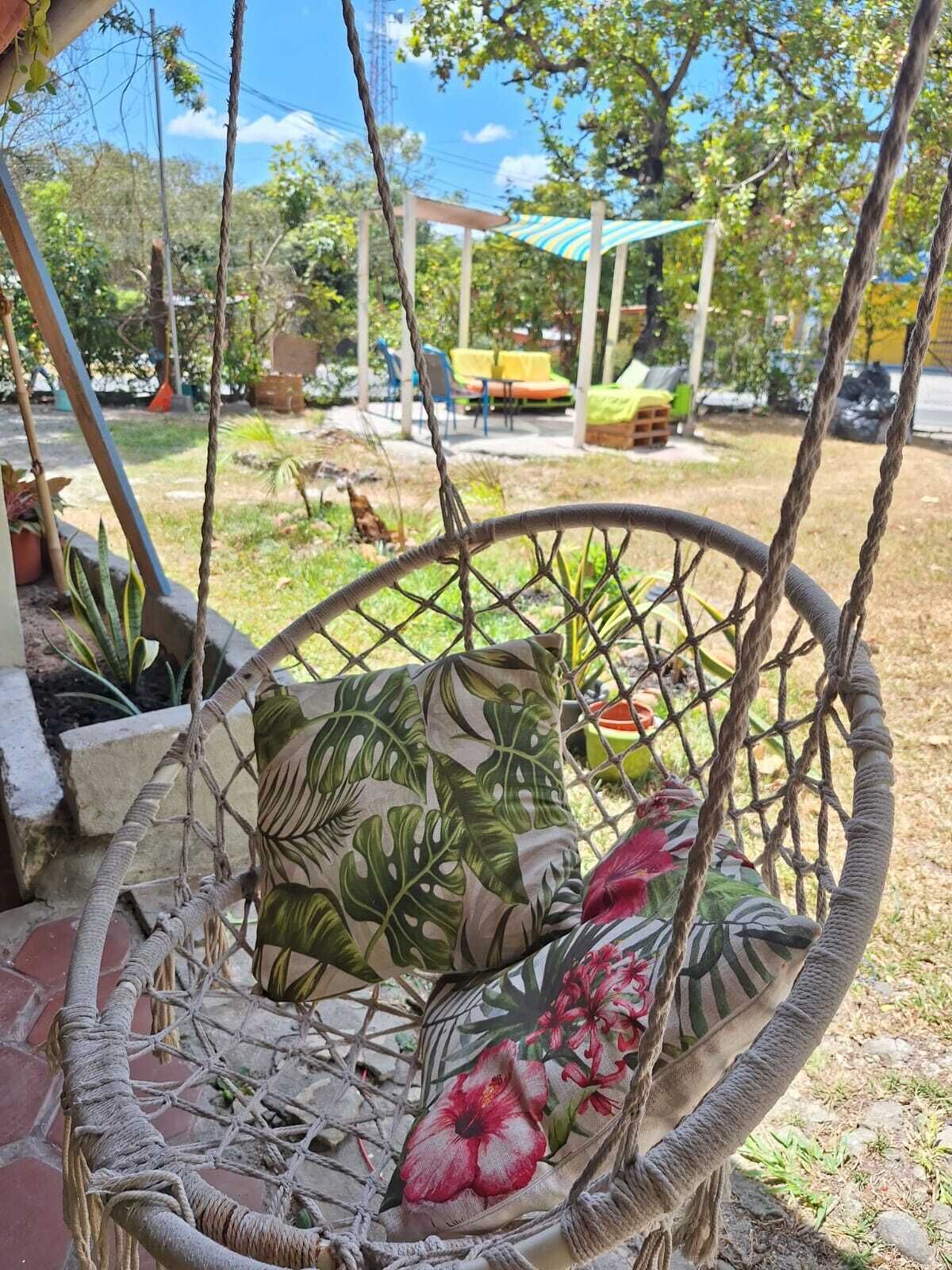 Una silla colgante con cojín floral, un espacio de patio con mobiliario exterior y vistas al jardín circundante.