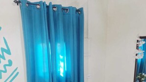 A room with two wooden chairs, a small white side table with a plant, and a blue curtain. - Acuarela Hostal - Hostel (Rio Hato)
