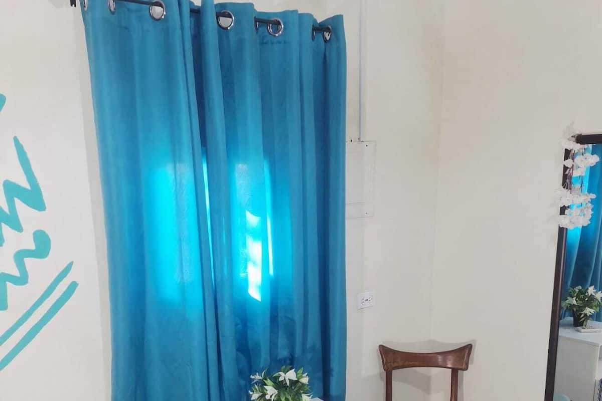 Una habitación con dos sillas de madera, una mesita auxiliar blanca con una planta y una cortina azul.
