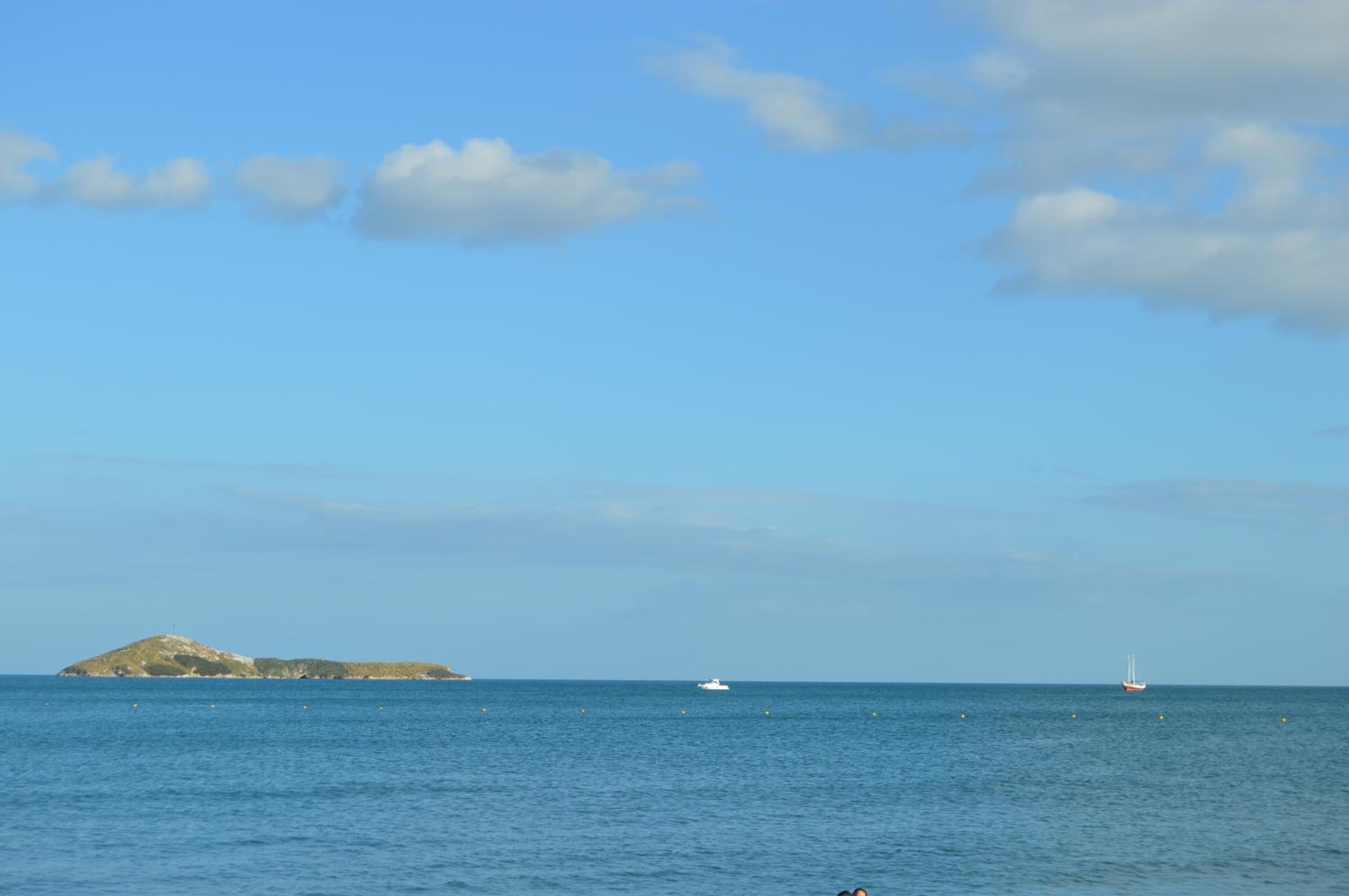 Mar tranquila con una pequeña isla y dos barcos a lo lejos.
