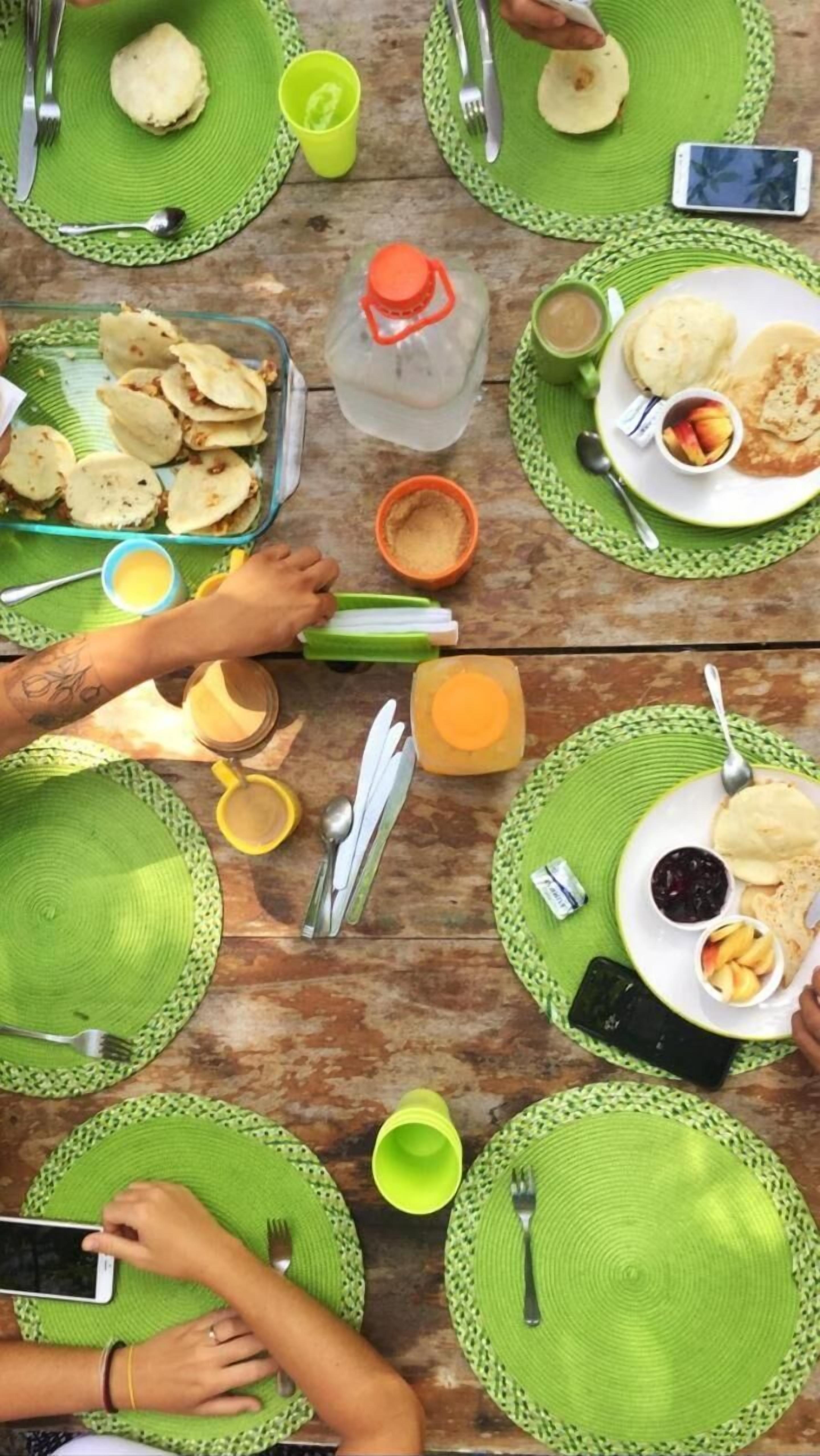 Una mesa de comedor con varios individuales verdes, platos con comida y diversos utensilios.