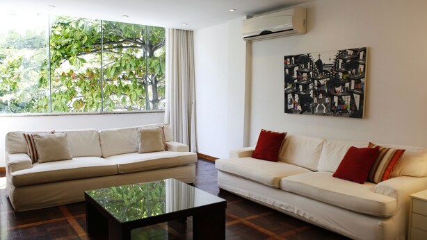 A modern living room with two white sofas, a glass coffee table, and a large window with a view of trees. - Rio045 - Apartment Ipanema (Rio de Janeiro)