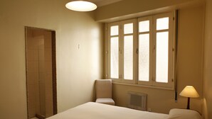 A hotel room with a bed, a chair, a window, and a radiator. - Rio045 - Apartment Ipanema (Rio de Janeiro)