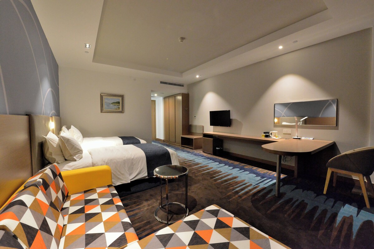 Une chambre d’hôtel avec un lit, un canapé, un bureau, une chaise, une télévision et un tableau au mur.