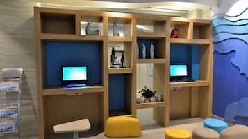 A modern room with wooden shelving units, two computers, a small table, and colorful ottomans.