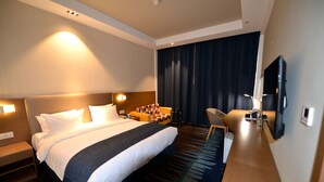 A hotel room with a large bed, a desk, a chair, a TV, and a window with curtains.