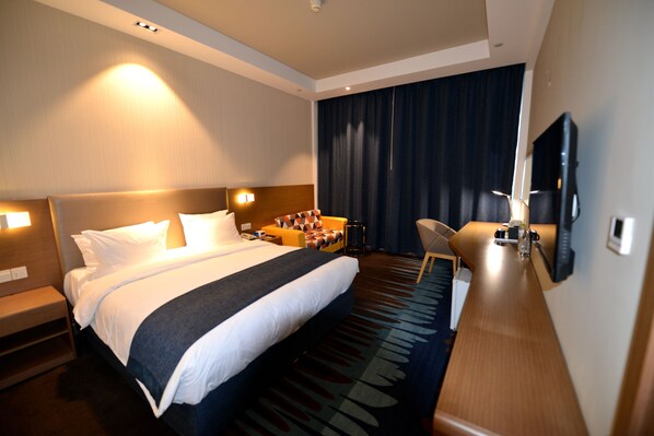 Une chambre d’hôtel avec un grand lit, un bureau, une chaise, une télévision et une fenêtre avec des rideaux.