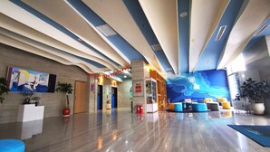 A modern lobby with a polished floor, a reception desk, a seating area with colorful cushions, and a large mural on the wall.