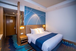 Une chambre d’hôtel avec un grand lit, une table de chevet, une lampe fixée au mur et une porte avec une pancarte.