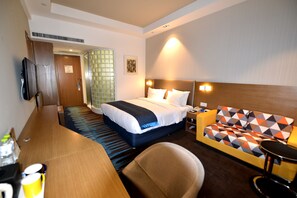 Une chambre d’hôtel avec un lit, un canapé, un bureau et une télévision.