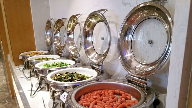 A buffet setup with various dishes in stainless steel chafing dishes, including a large bowl of sausages.