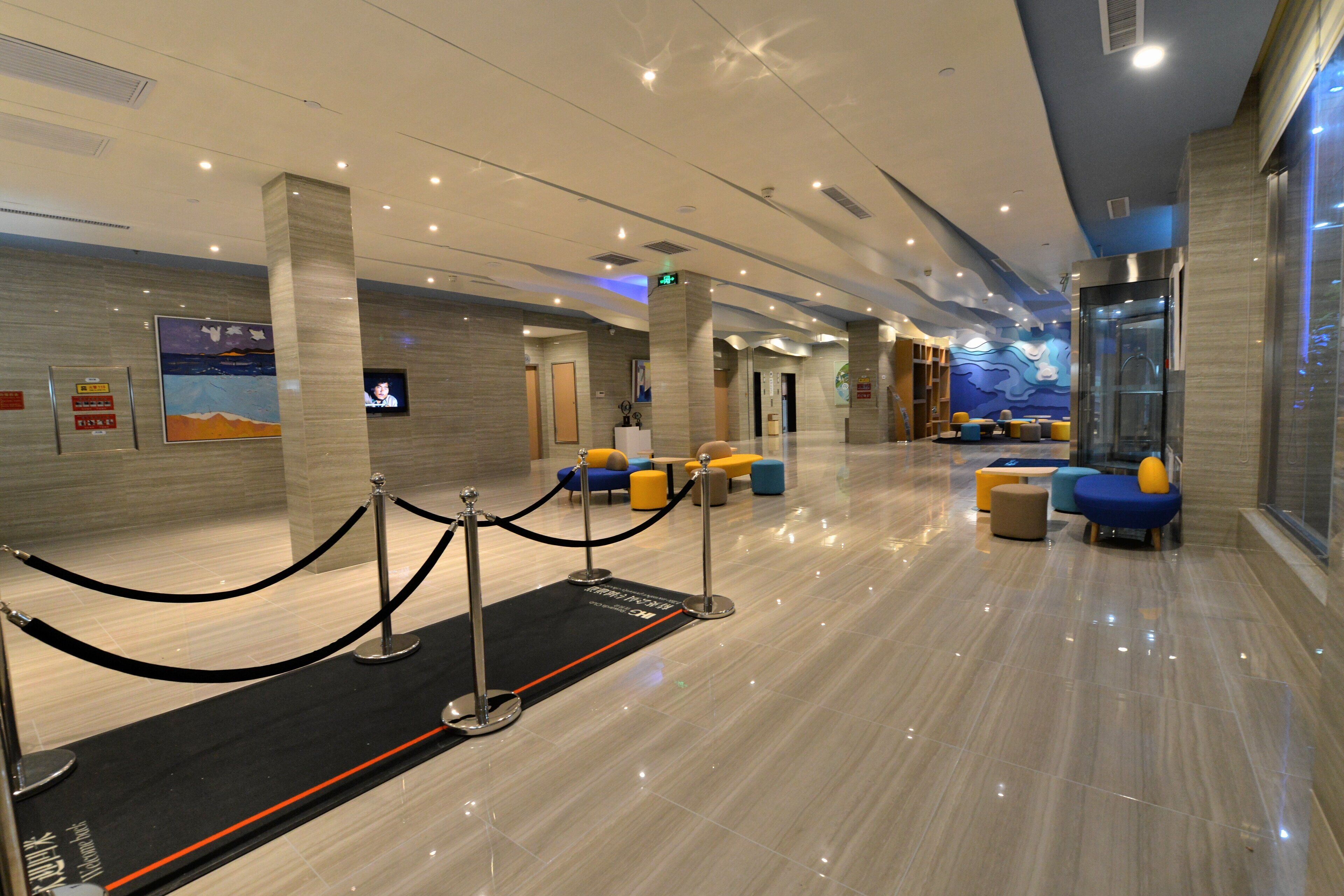 A modern hotel lobby with a reception desk, seating area, and a glass elevator.