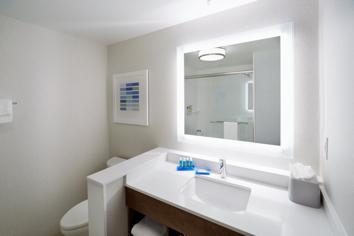 A modern bathroom with a white sink, mirror, and toilet. There is a towel rack and a framed color chart on the wall.