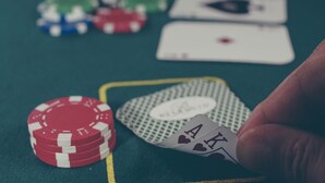 A hand holding a playing card with a heart symbol, a stack of red poker chips, and a green playing card on a green surface. - Holiday Inn Express & Suites-Cincinnati North - Liberty Way by IHG (West Chester)