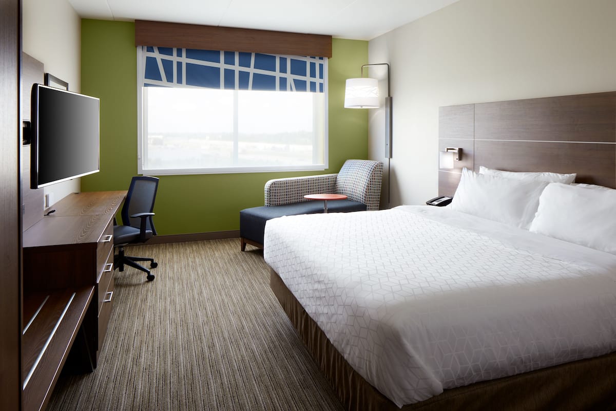 A hotel room with a large bed, a desk with a flat-screen TV, a chair, and a window with a view.