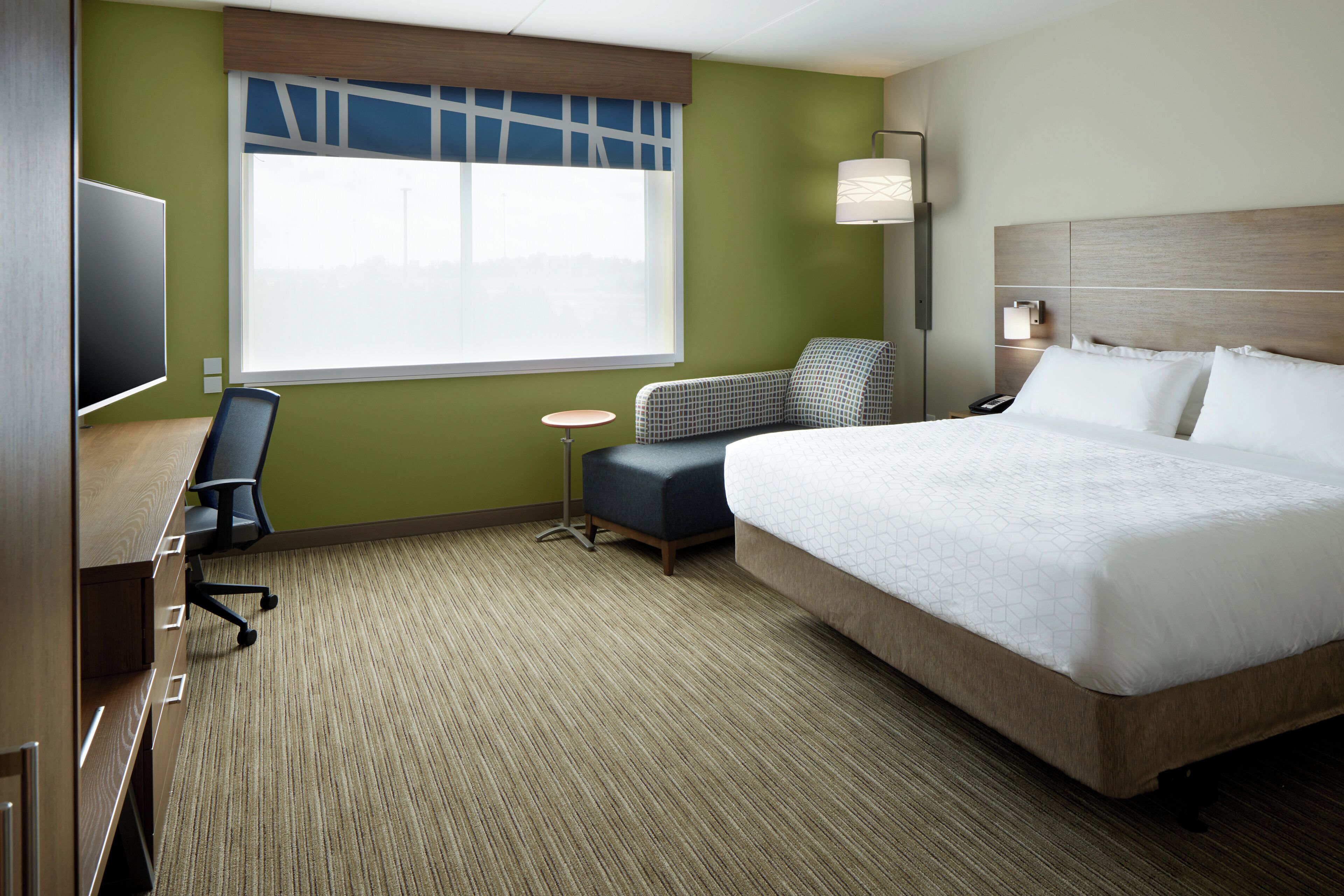 A hotel room with a large bed, a desk with a chair, a small round table, and a television.